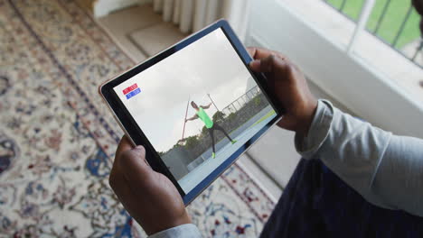 compuesto de un hombre sentado en casa, viendo el evento de jabalina de atletismo en la tableta