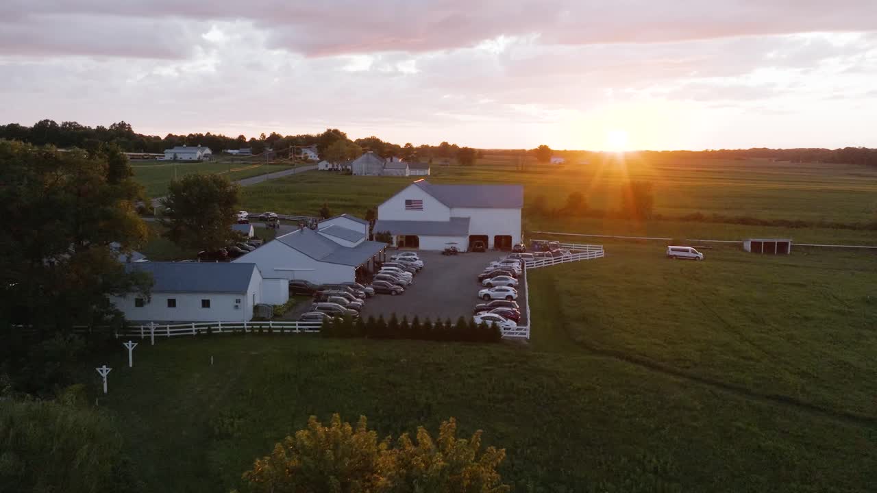 En fantastisk udsigt over en solnedgang fra et dronebillede af en smuk gård og omkringliggende grønne græsgange og hvid lade