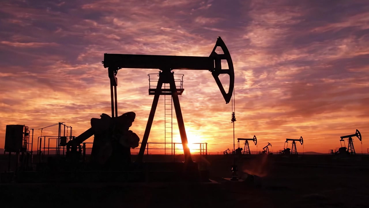 Dramatic Sunset Over Oil Pumps: A Striking Display of Industry Silhouetted Against Vibrant Skies, Capturing the Essence of Energy Production at Dusk.