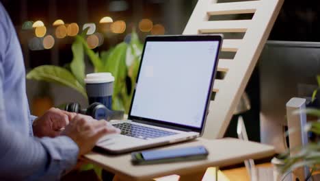 sección media de un hombre de negocios biracial usando una computadora portátil con espacio de copia en la oficina por la noche, en cámara lenta