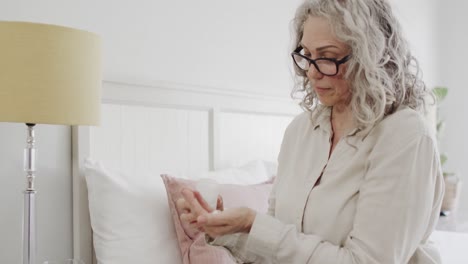 Mujer-Caucásica-Mayor-Con-Gafas-Sentada-En-La-Cama-Y-Tomando-Tabletas-Medicinales,-Cámara-Lenta