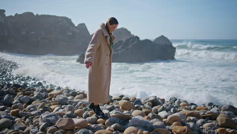 girl walking beach stones in sunlight. thoughtful traveler balancing rocky beach