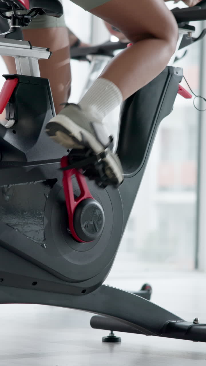 Primer plano de piernas pedaleando en una bicicleta estática en un gimnasio.