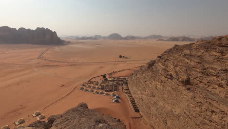 Wadi-Rum,-Jordania,-Vista-Panorámica-Del-Paisaje-Desértico,-Acantilados-Escarpados-Y-Campamento-Beduino-En-Un-Día-Caluroso-Y-Soleado