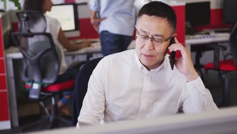 senior businessman talking on his smartphone while sitting on his desk in office in slow motion