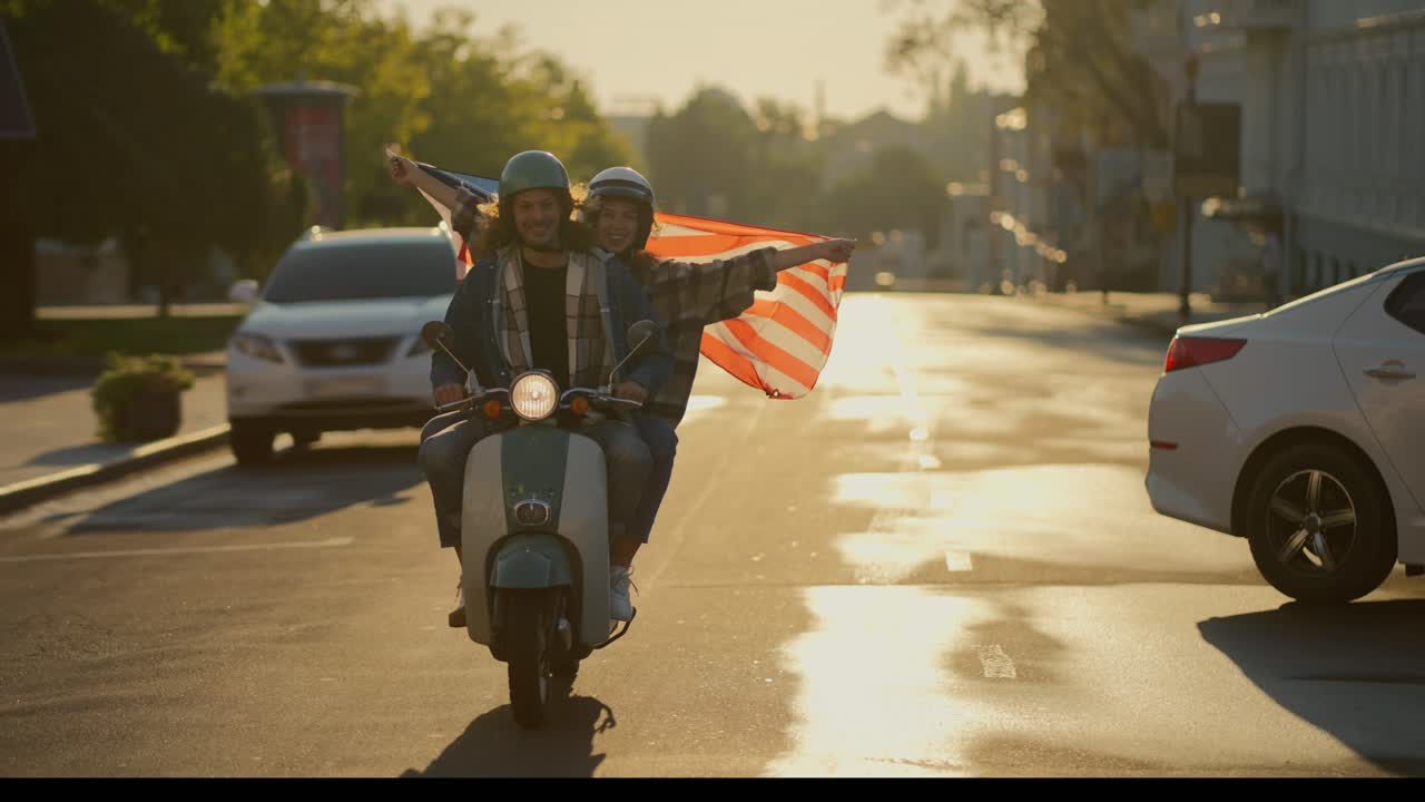 Happy couple, a brunette guy with curly long hair in a denim jacket and his girlfriend in a plaid shirt holds a large USA flag, which flutters beautifully in the wind while driving through a summer city in the morning