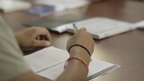 a student tries to answer a test, close-up on the hand, the student plays with the pen, and he has a bracelet on hand