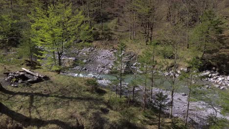 Drones-Vuelan-Lentamente-Pasando-Por-La-Fogata-Con-Un-Hermoso-Río-De-Montaña-Turquesa-En-El-Fondo-En-Austria,-Europa