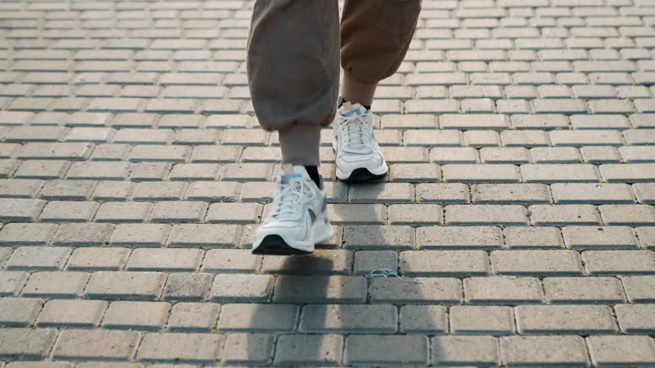 Caucasian man stepping forward on textured brick pavement in white trainers, closeup front view of foot landing, soft sunlight casting long shadow, confident pace in city streetwear scene