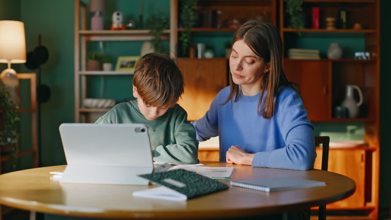 Madre che aiuta con l'istruzione online spiegando un compito scolastico a uno scolaro attento.