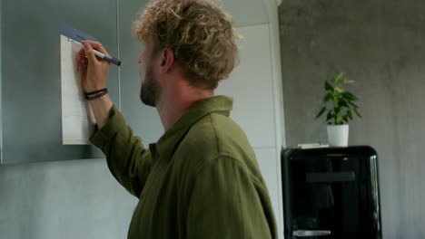 man writing on a kitchen calendar