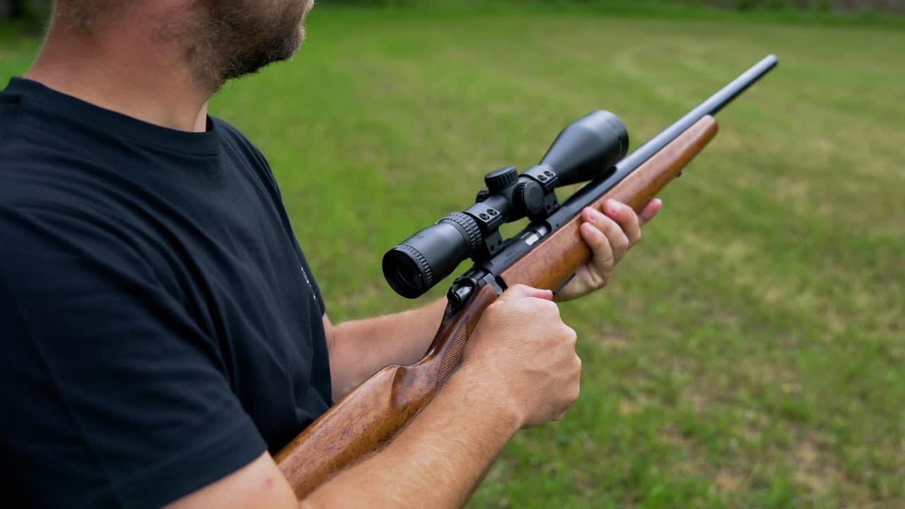 Middle aged white Caucasian man cocks cabin of hunting snipers rifle made of wood and metal and takes aim down the scope before firing at a shooting range