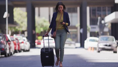 African-american-woman-using-smartphone-and-wheeling-in-city-street