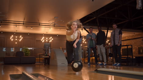 a young woman in bowling throws a ball on the track and knocks out a shot in slow motion and jumps and dances for joy. friends fans support and clap with a smile.