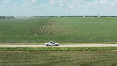 Aerial-side-view,-white-pickup-truck-driving-on-rural-countryside-unpaved-farm-road