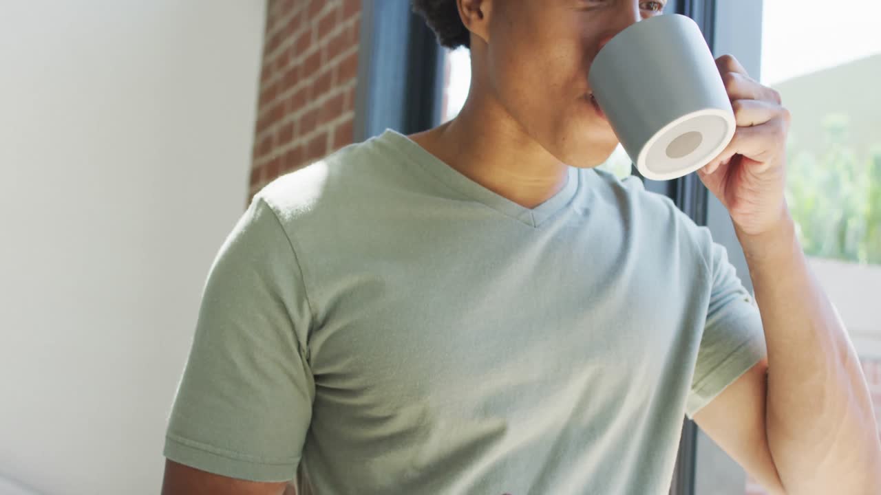 아프리카계 미국인 남자가 집에서 스마트폰을 사용하고 커피를 마시고 있습니다.