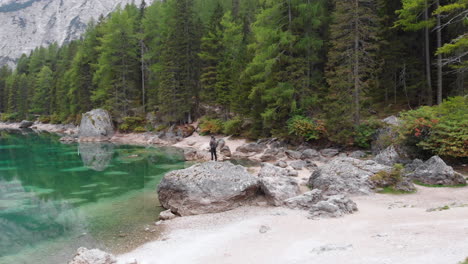 backwards revealing drone shot of a male model standing on a rock overlooking lake braies in the dolomites, italy