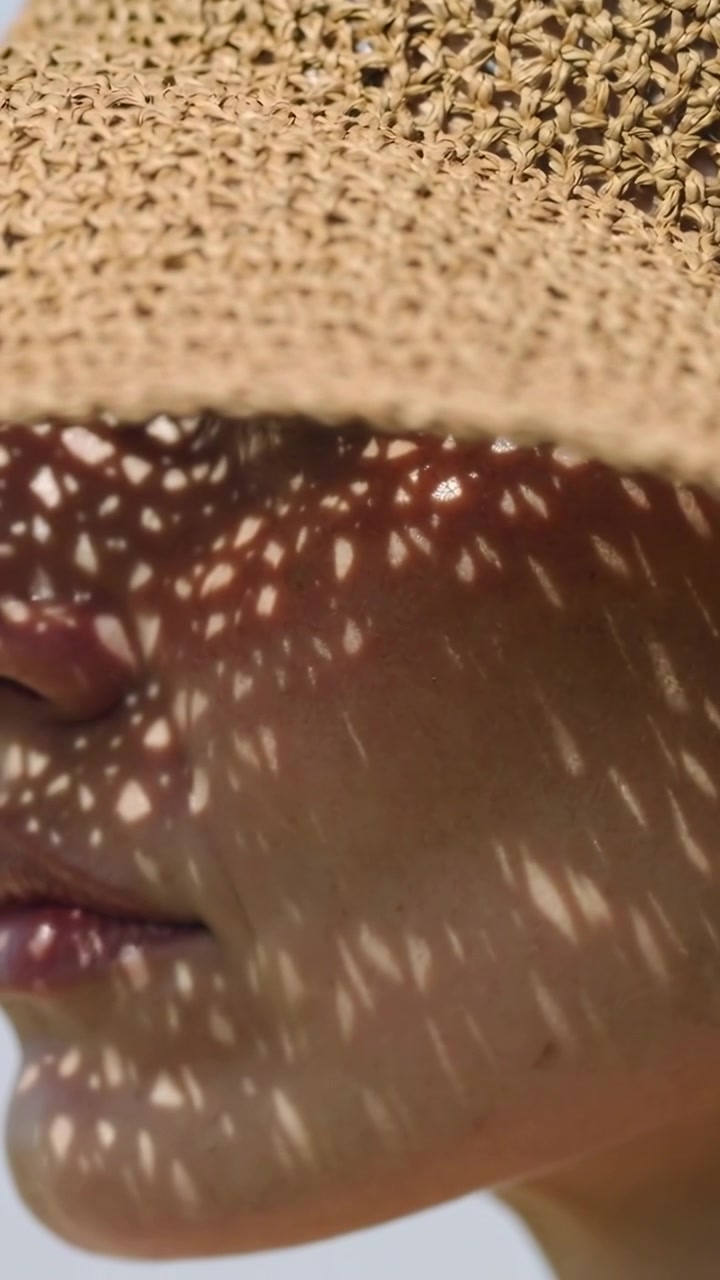 Video verticale: Donna che si inclina, con cappello di paglia sotto il sole intenso, la mano sinistra tocca la tesa per ombreggiare gli occhi.