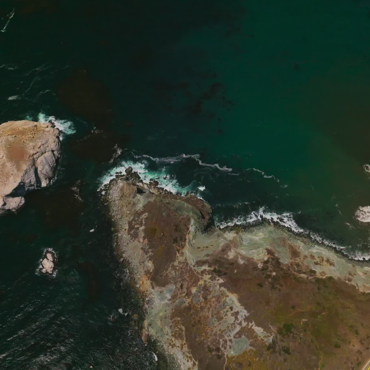 Mountainous landscape crossed by roads with moving cars. Sea-green water of Pacific ocean washing the bare rocks. Sunny day footage