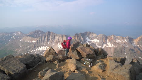 lonely woman on mount sneffels 14er summit, hiker with backpack and helmet atop peak with incredible view on mountain range, colorado usa