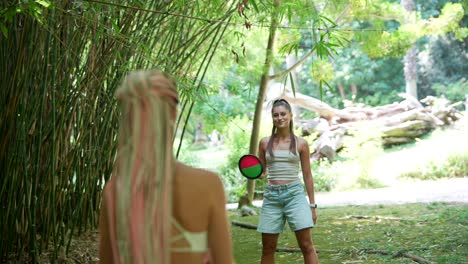 two women playing frisbee in a bamboo grove