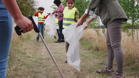 líderes de equipos adultos con un grupo de niños en un campamento de actividades al aire libre recolectando basura juntos