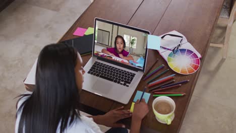 African-american-female-teacher-writing-on-memo-notes-having-a-video-call-on-laptop-at-home