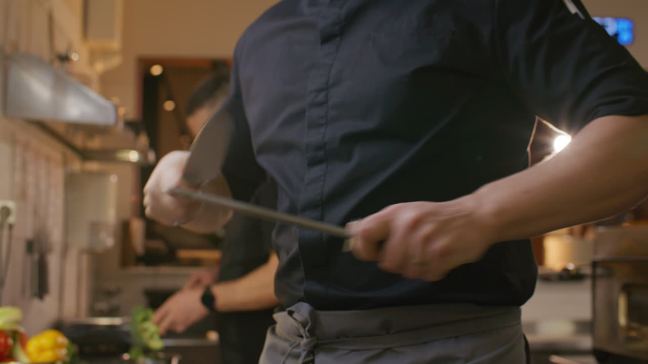 Chef del ristorante che affila un coltello da cucina con un acciaino.