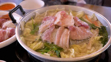 steaming hot pot filled with thinly sliced meat and loads of vegetables, cooked on a stove top using induction heat