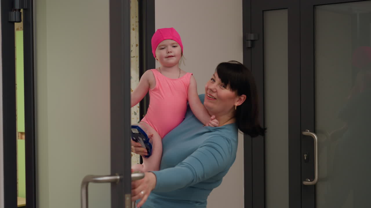 Nanny carrying child while opening door, hand on knob, soft indoor light, gentle smile, warm care, secure hold, profile view, calm hallway scene, entering room with patient guiding posture