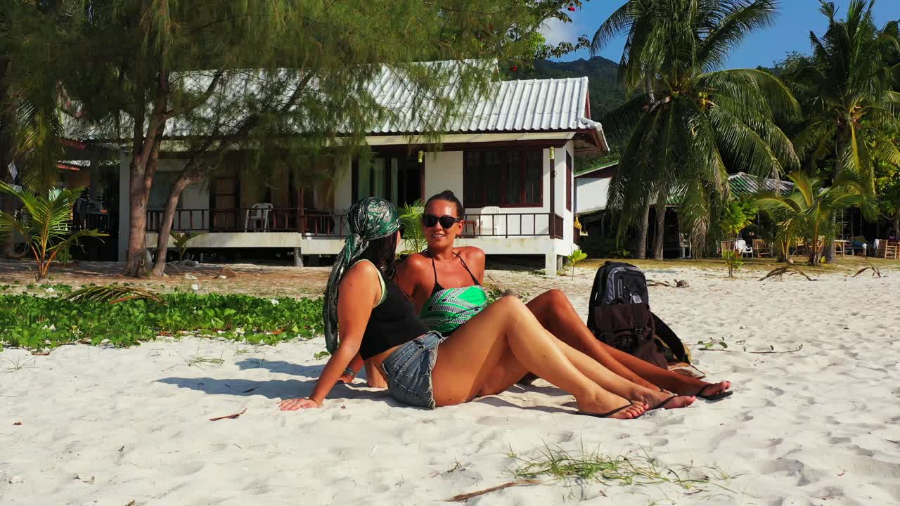 Model girls just arrived on paradise exotic beach sitting on white sand, watching beautiful sea and mountains horizon in Thailand