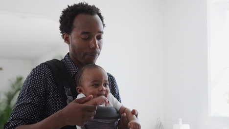 father playing game with smiling baby son in sling at home