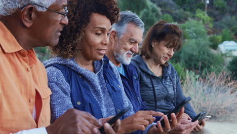 group of senior friends on hike in countryside checking mobiles phones for fear of missing out