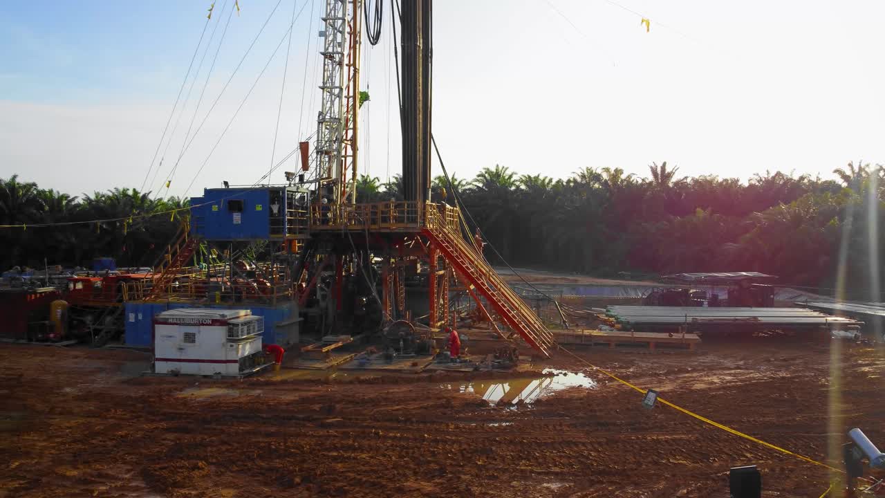 imágenes cinematográficas de drones de 4k de la estructura del equipo de la plataforma de perforación en tierra para la exploración y explotación de petróleo en medio de la jungla rodeada de palmeras durante la puesta de sol y el alto precio del petróleo