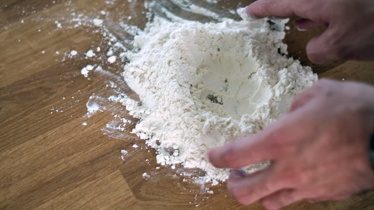 Man's hands carefully making a hole in flour mound