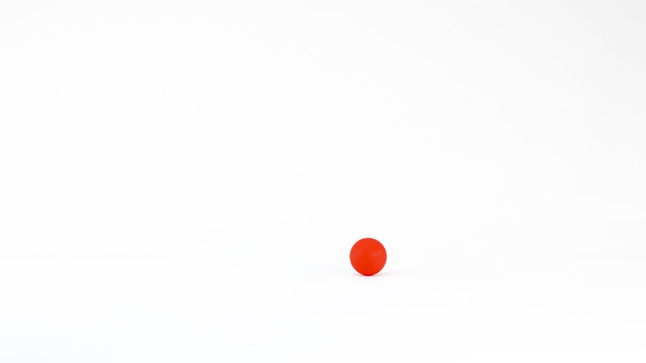 A single red sphere rolls smoothly across a bright white surface in a studio setting