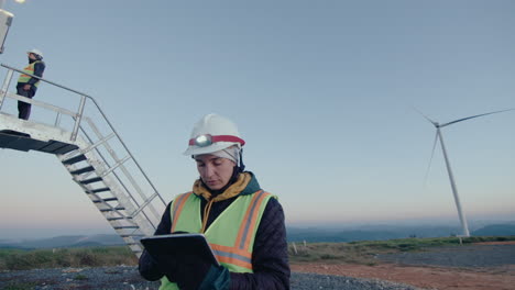 female technician inspecting wind power plant with tablet
