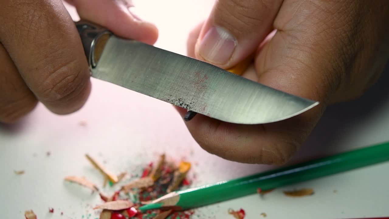 imágenes de manos afilando lentamente un lápiz y algunos lápices de colores con un cuchillo afilado