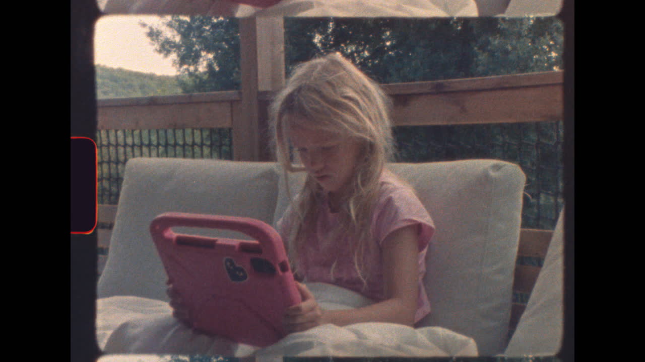 Young blonde girl cozied up with tablet on porch