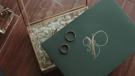 close up of two wedding bands placed on green envelope with monogram beside flower box