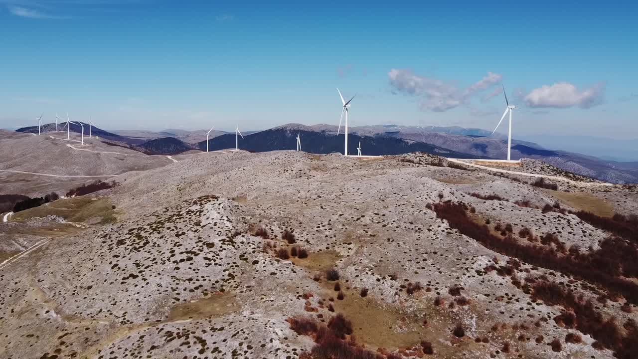 toma aérea de las montañas griegas con una moderna granja de turbinas eólicas contra el cielo azul - toma de establecimiento de drones