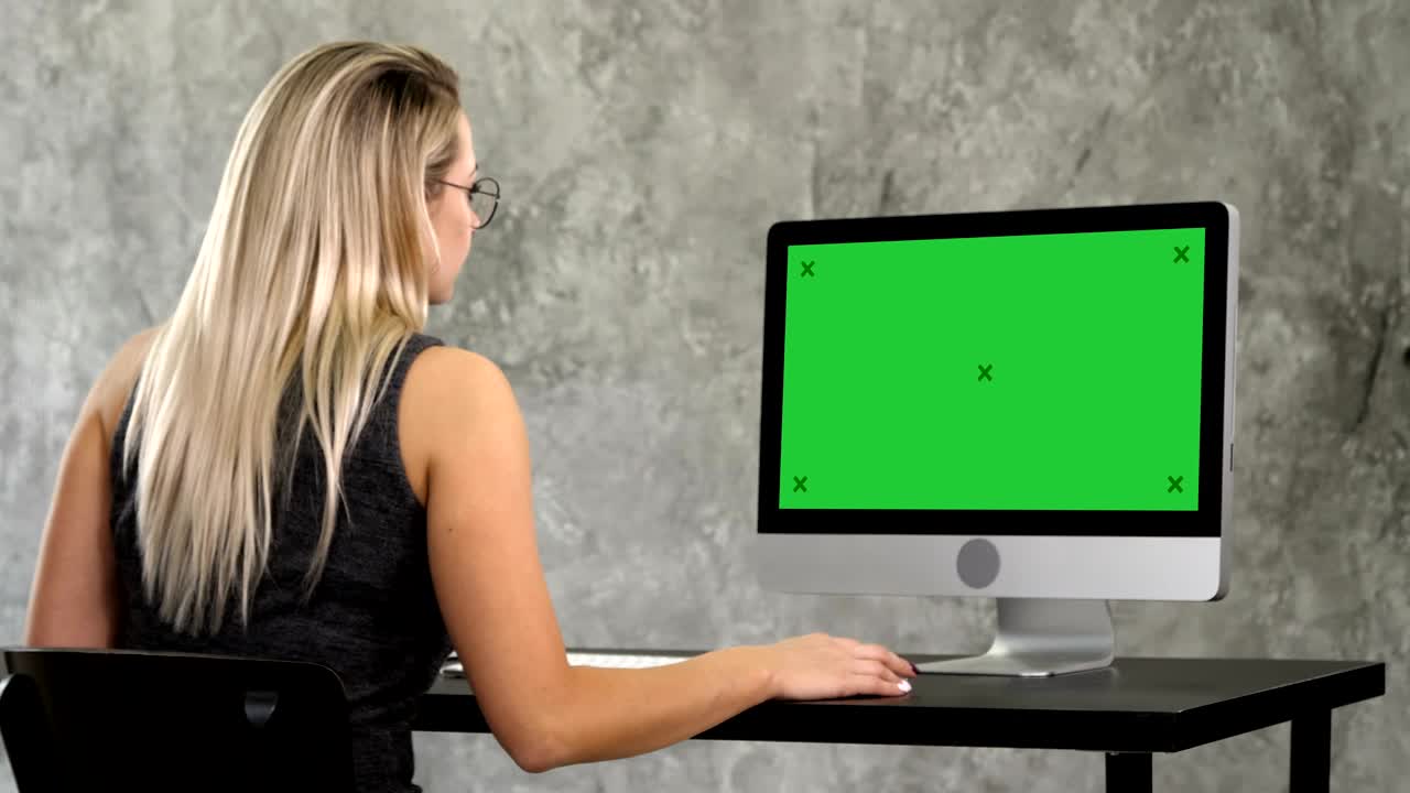 chica hipster con gafas de moda se sienta en la mesa frente a la computadora trabajando. pantalla verde muestra de maqueta