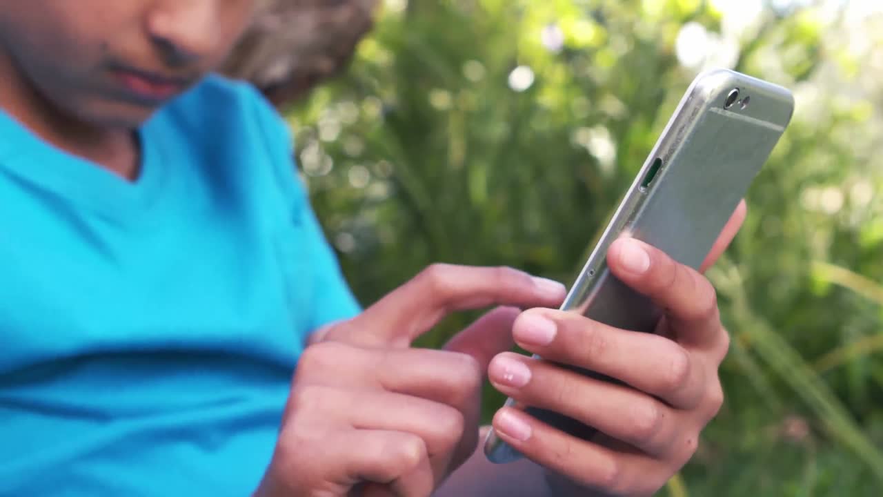 un niño lindo usando un teléfono inteligente sentado en el césped