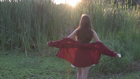 back view of young woman walking with flower in his hand sunlit at sunset