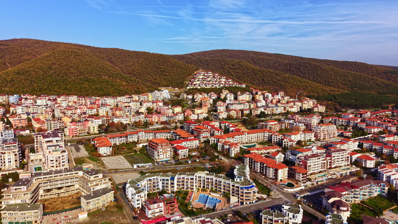 Živá obytná oblast uhnízděná v bujných zelených kopcích za slunného odpoledne představuje moderní architekturu a komunitní život.