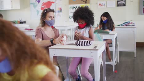 female teacher and girl wearing face masks sanitizing her hands at school