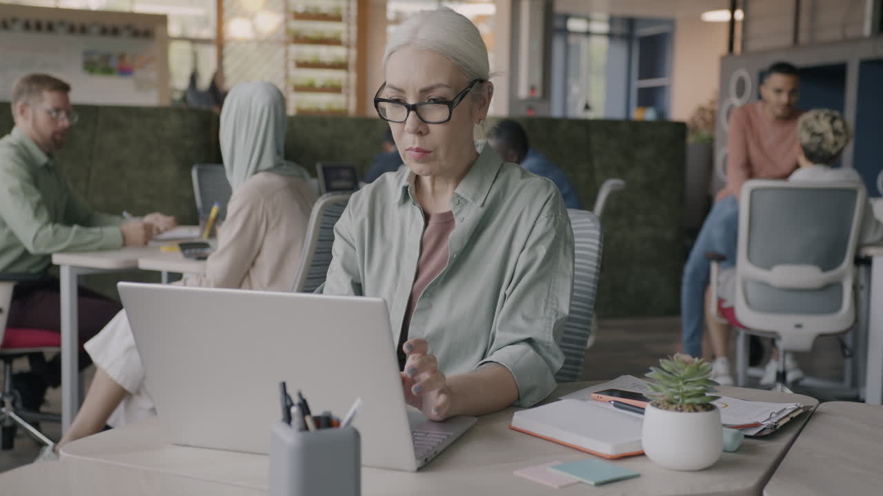 Senior Woman Working on Laptop in Modern Open-Plan Office