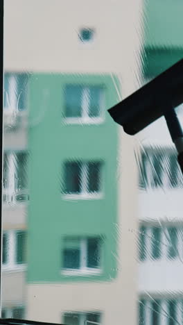 process of washing window at home in the city. silhouette of a man cleaning glass window with a brush and special liquid in flat on high building background. vertical video
