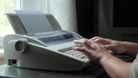 person types on a typewriter next to a window in slow motion