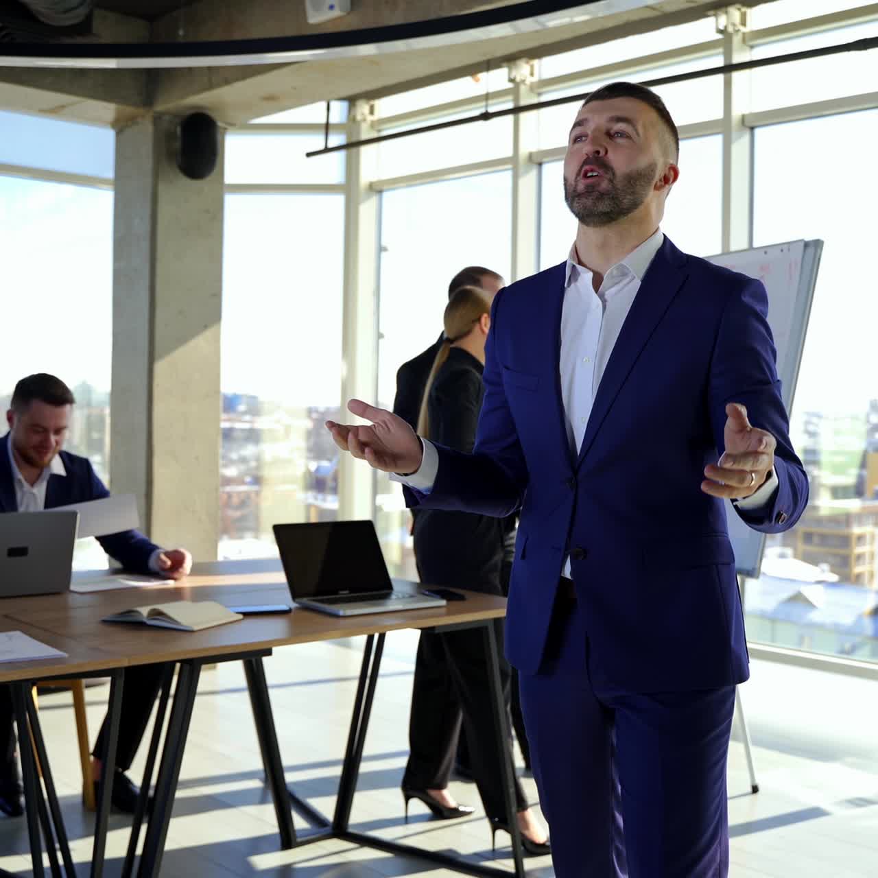 People work in office. Elegant businessman in suit talking on camera. Men and women entrepreneurs working in groups in modern office center in the city